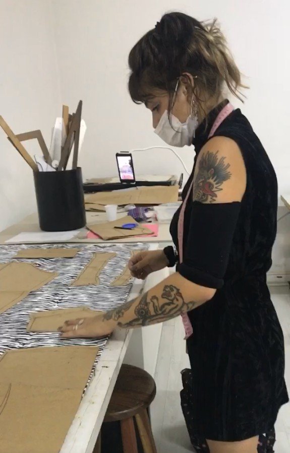 Aluna posiciona molde de modelagem sobre tecido para iniciar corte de camisa feminina sob medida em aula de costura
