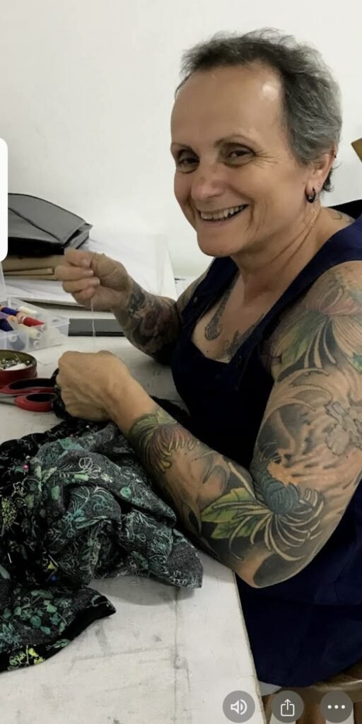 Aluna sentada à mesa alinhavando peça em aula prática de costura