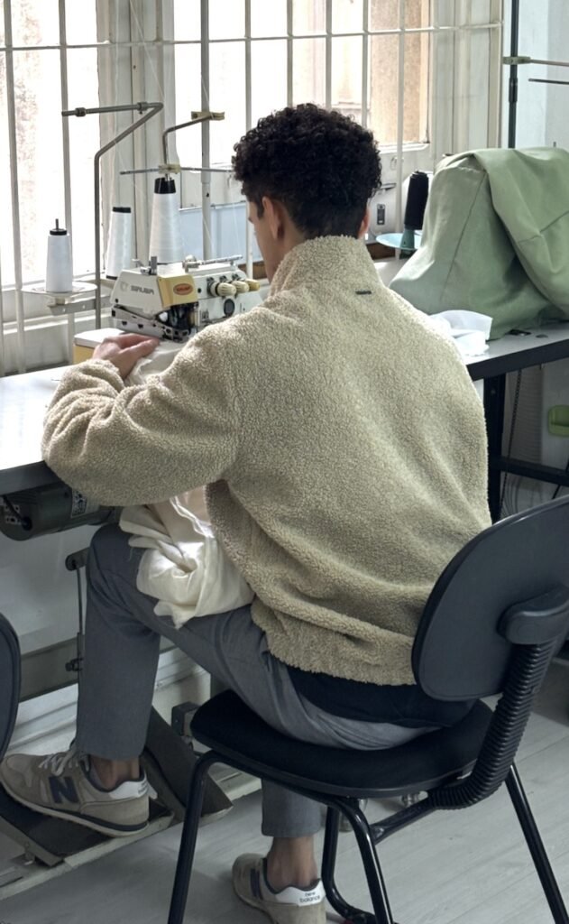 Aluno em aula prática de costura na Escola de Moda Paulistana, utilizando máquina overloque