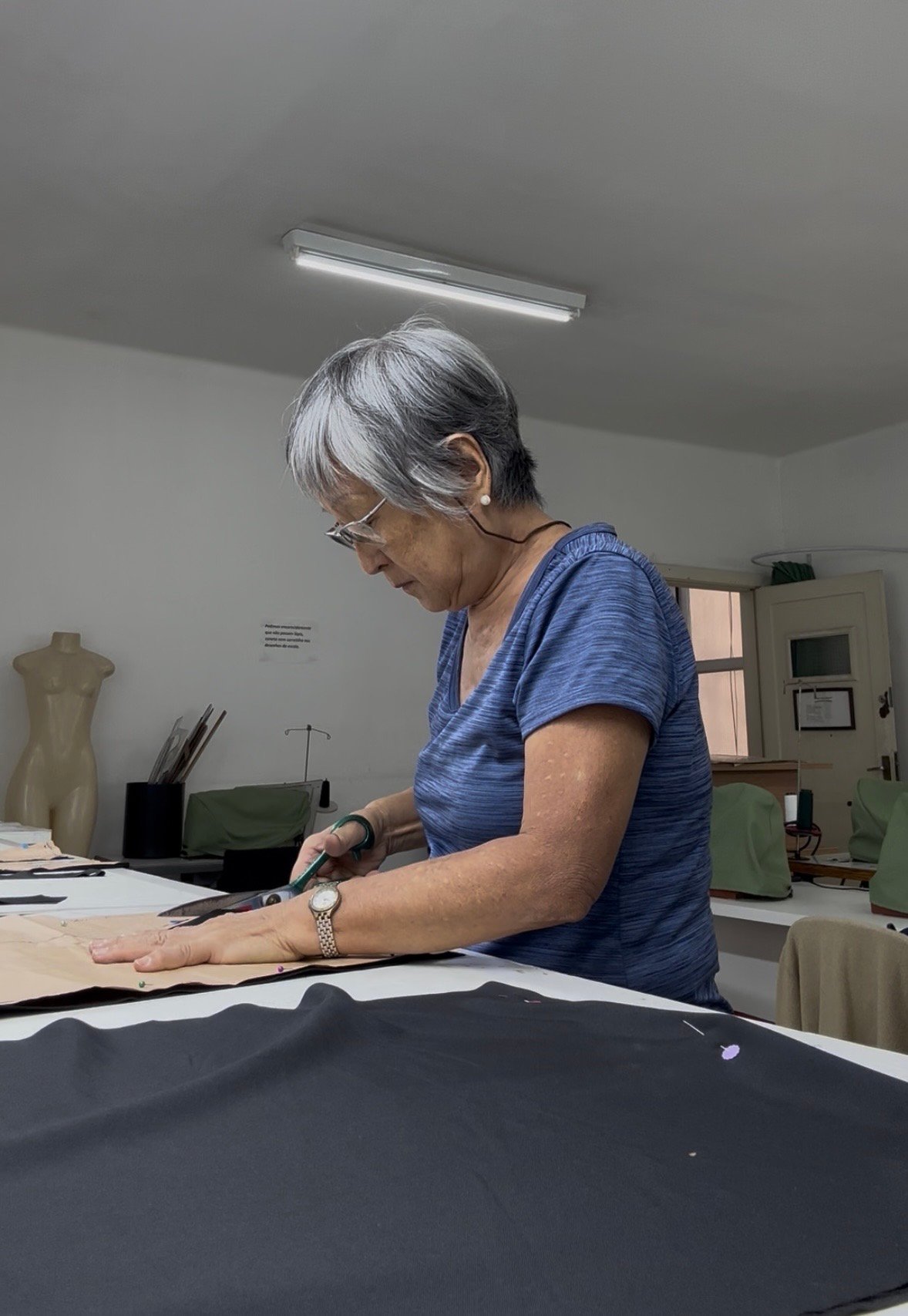 Aluna do curso de corte e costura da Escola de Moda Paulistana cortando tecido em aula prática em São Paulo